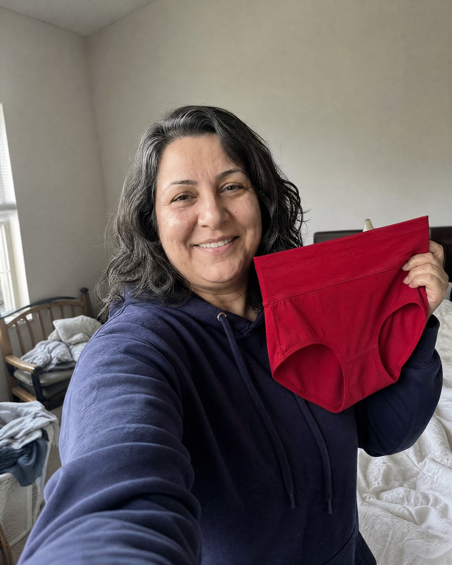 Smiling woman holding up a burgundy Jadea brief in a selfie