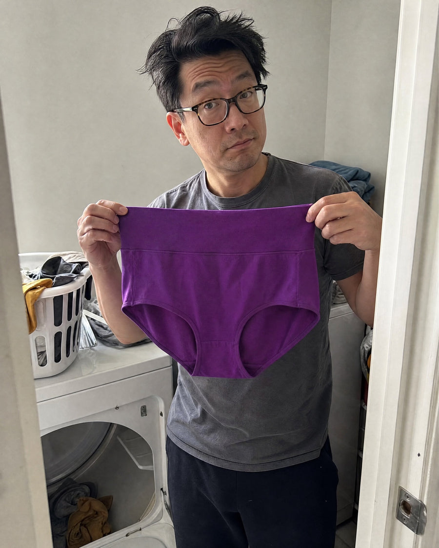 Husband holding up a purple Jadea brief by the dryer, impressed